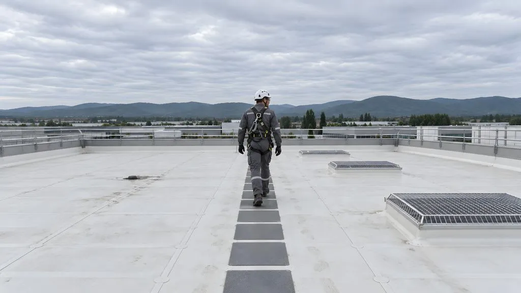 Operatore con casco e imbracatura su copertura piana in TPO messa in sicurezza con parapetto e lucernari protetti da griglie